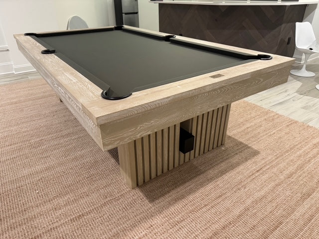 Modern pool table with wooden finish and dark felt surface in a room setting.