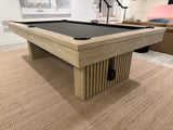 Wooden pool table with a black felt surface in a room with a staircase and furniture.